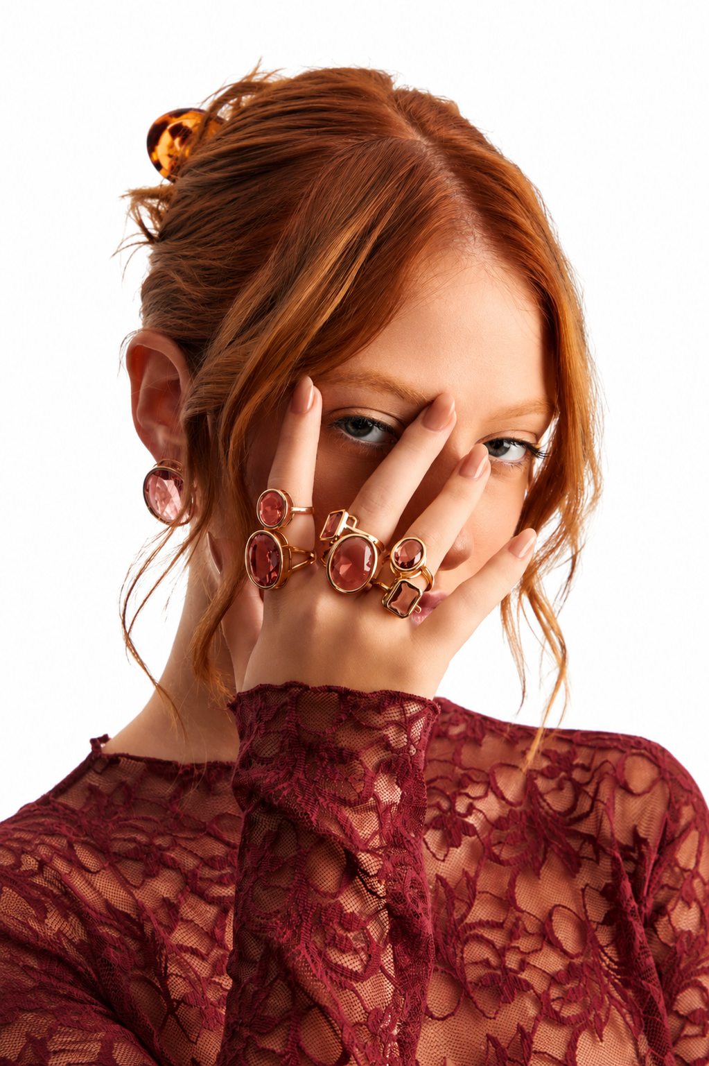 Woman wearing gold rings with a pink kristal and a red lace top on a white background 