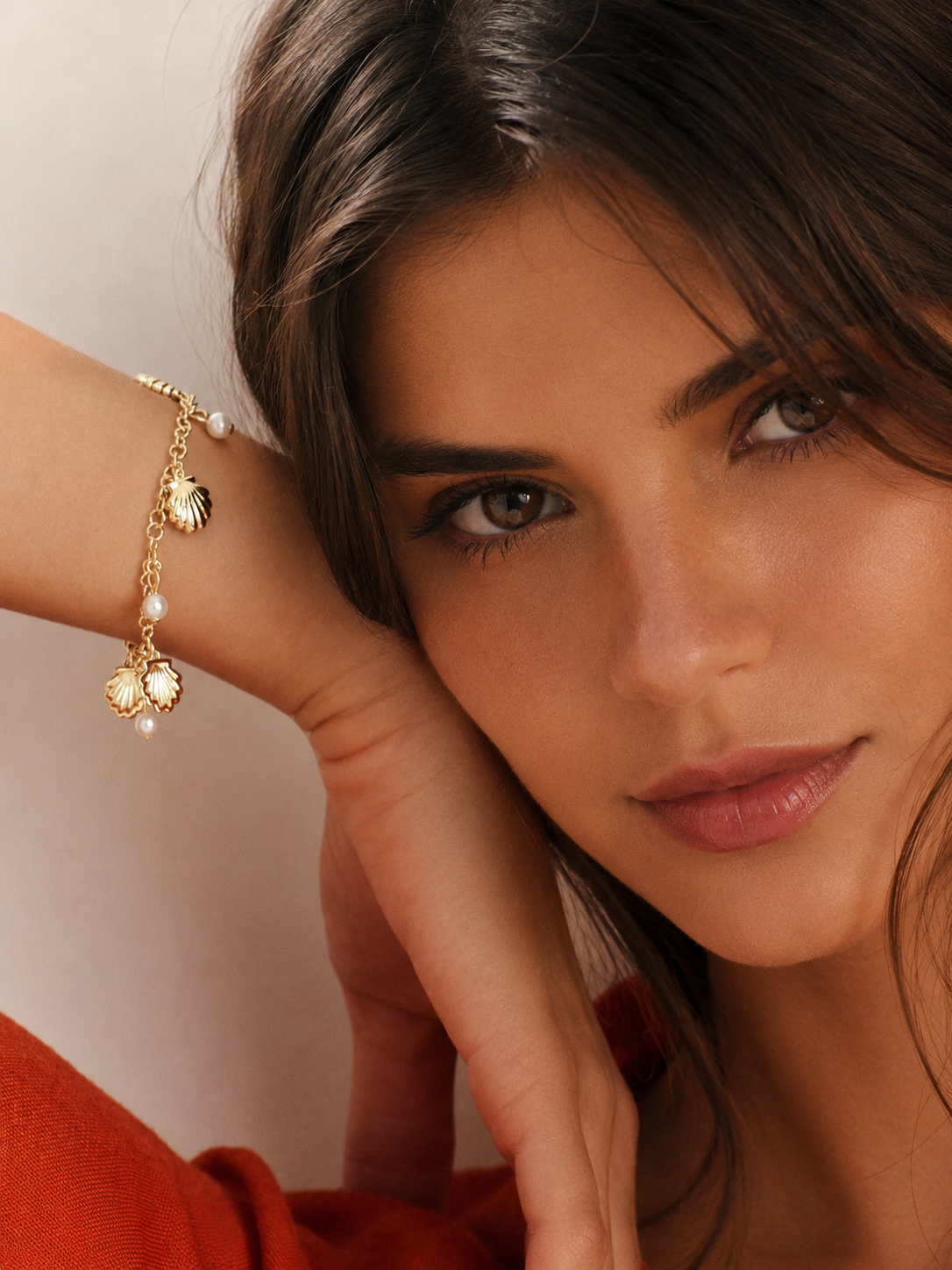 Woman wearing a gold bracelet with shell charms on a neutral background