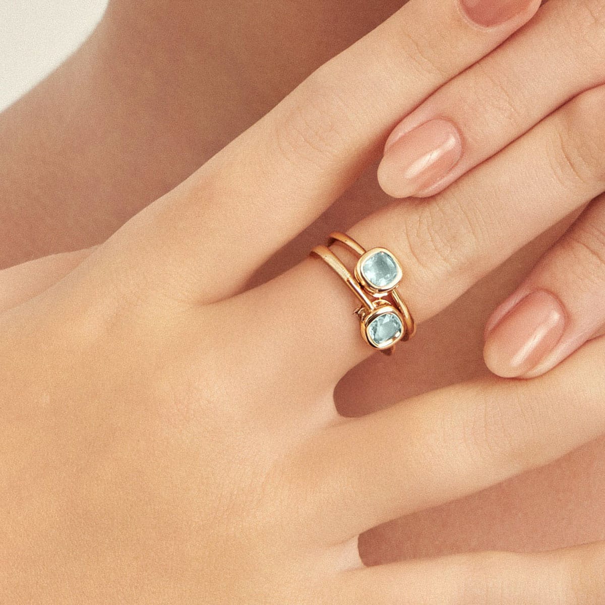 Delicate 18K gold-plated blue crystal ring with a cushion-cut stone worn on a woman's hand.